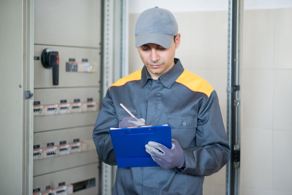 Electrician Writing a Document While Inspecting a Panel